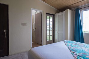 Une chambre à coucher avec un lit, une porte donnant sur une salle de bain et une fenêtre avec des rideaux.