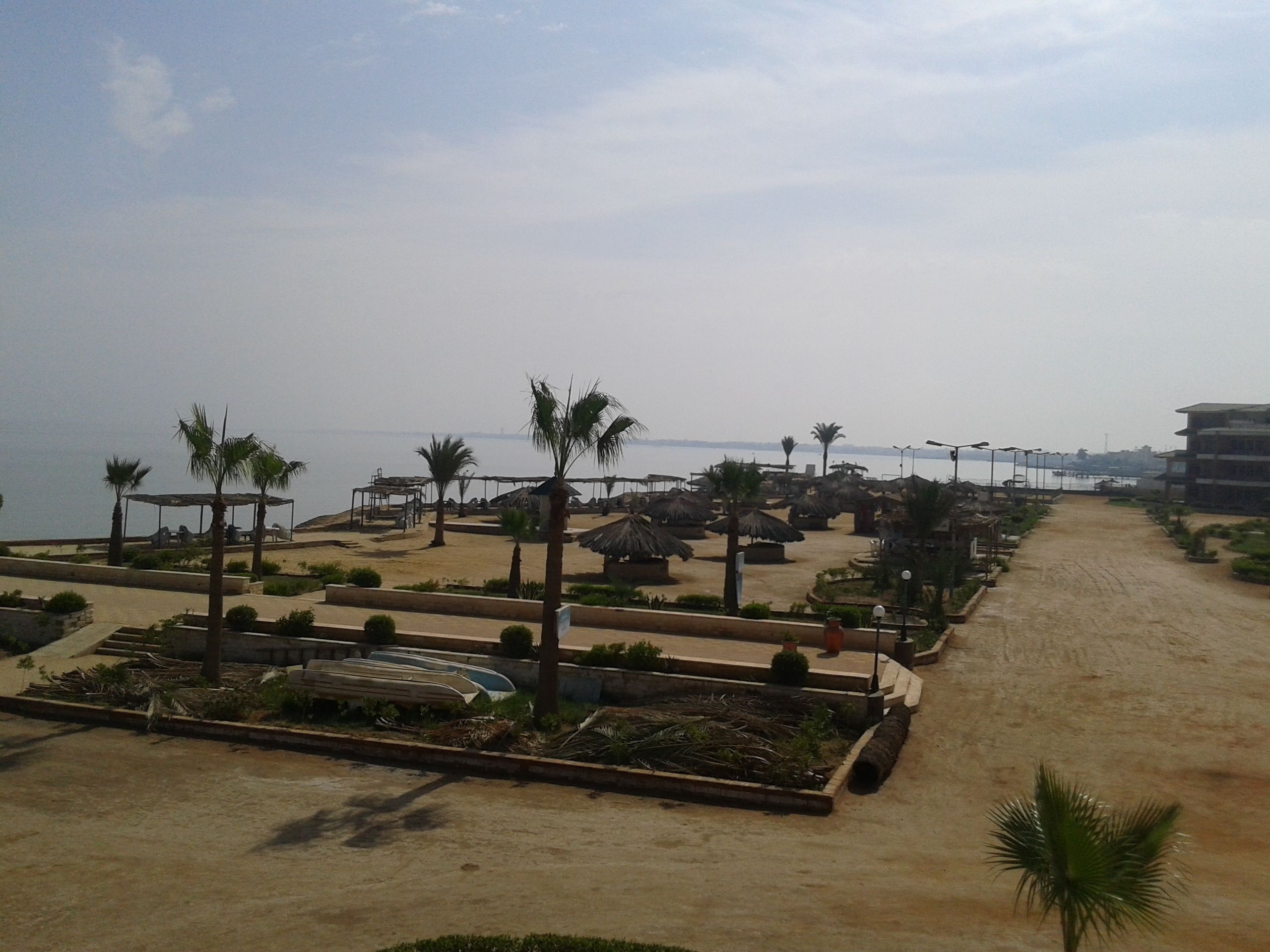Un complexe hôtelier situé en bord de mer, doté de bâtiments à toits de chaume, de palmiers et offrant une vue dégagée sur l’océan.