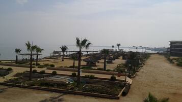 A beachside resort with thatched-roof structures, palm trees, and a clear view of the sea.