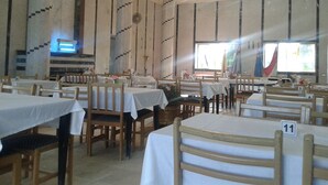 Un espace repas comprenant plusieurs tables et chaises, des places numérotées et une grande fenêtre laissant entrer la lumière naturelle.