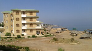 Un immeuble à plusieurs étages doté d’un toit végétalisé, entouré d’un espace paysager agrémenté de palmiers et de constructions à toits de chaume.