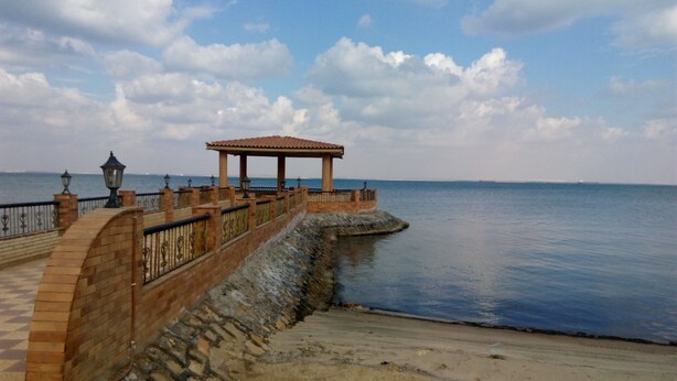 A coastal walkway with a stone railing, a covered pavilion, and a calm sea in the background. - Fayed Armed Forces Hotel (Fayed)