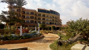 A multi-story hotel with a curved facade, a landscaped garden with pathways, and a large tree in the foreground. - Fayed Armed Forces Hotel (Fayed)