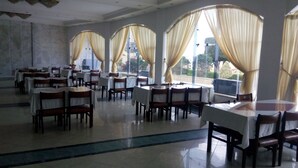 A spacious dining area with multiple tables and chairs, large windows with curtains, and a view of the outdoors. - Fayed Armed Forces Hotel (Fayed)