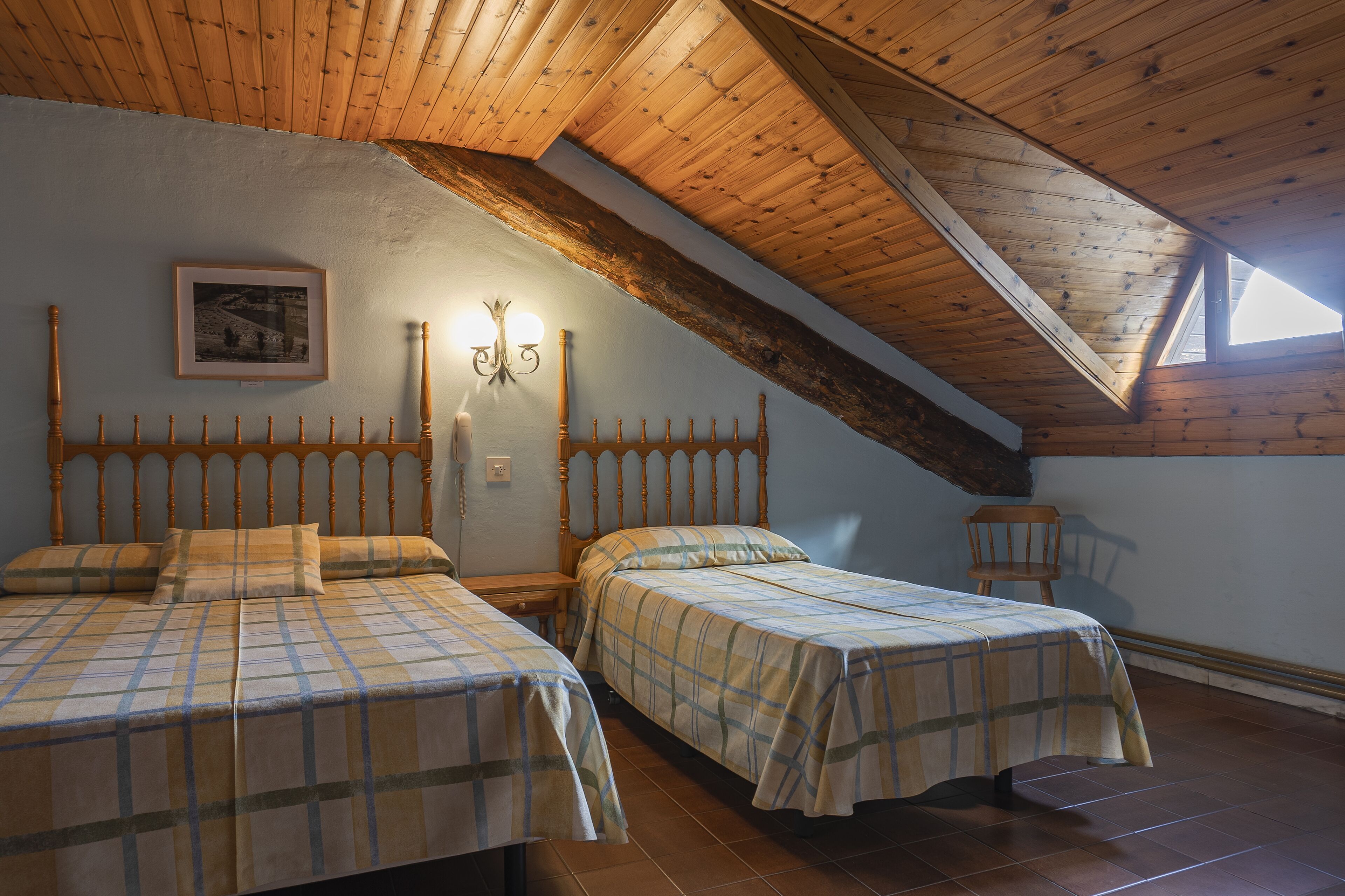 A bedroom with two beds, wooden headboards, a framed picture on the wall, and a sloped ceiling.