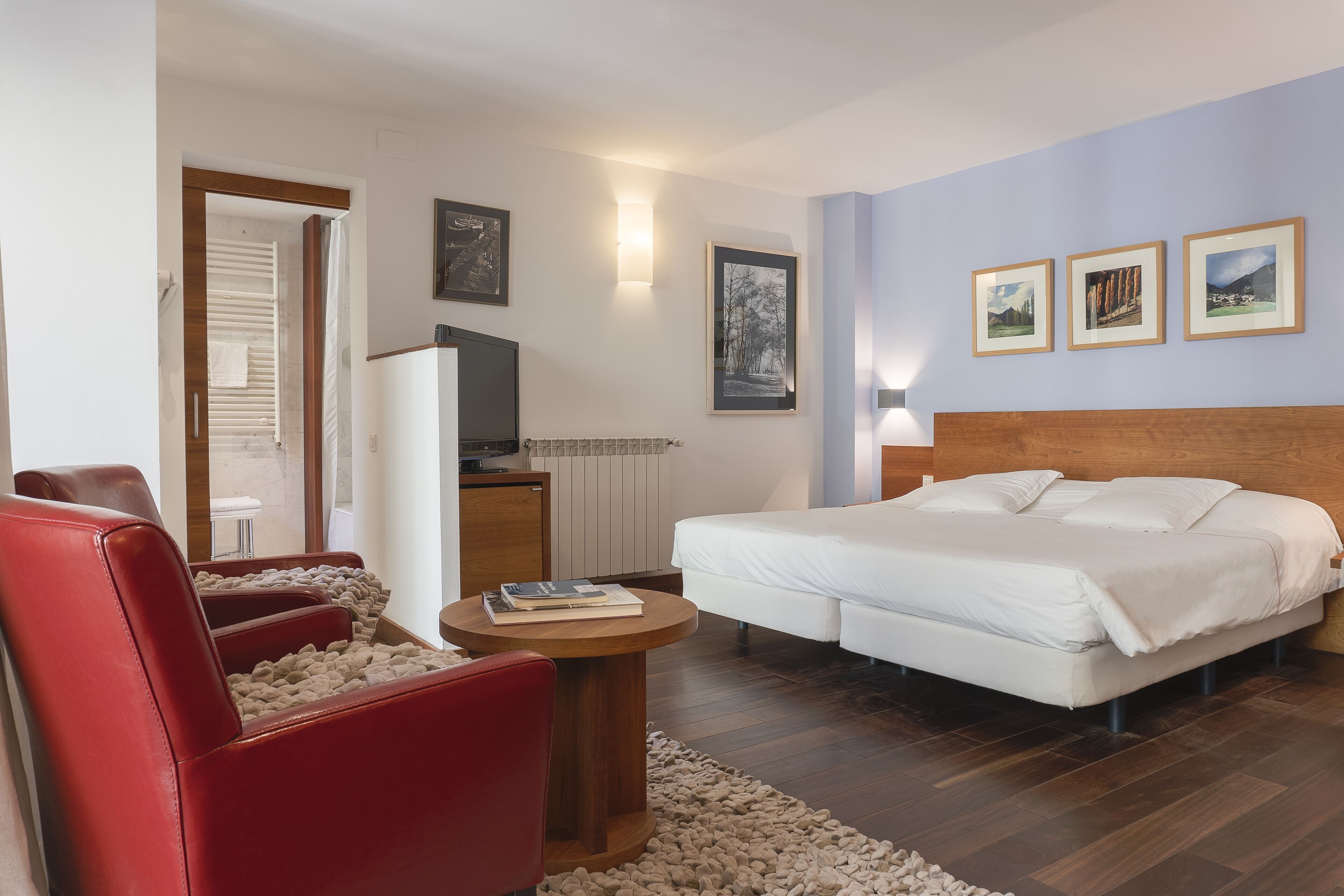 Une chambre d’hôtel avec un lit, un fauteuil rouge, une petite table ronde et un téléviseur.