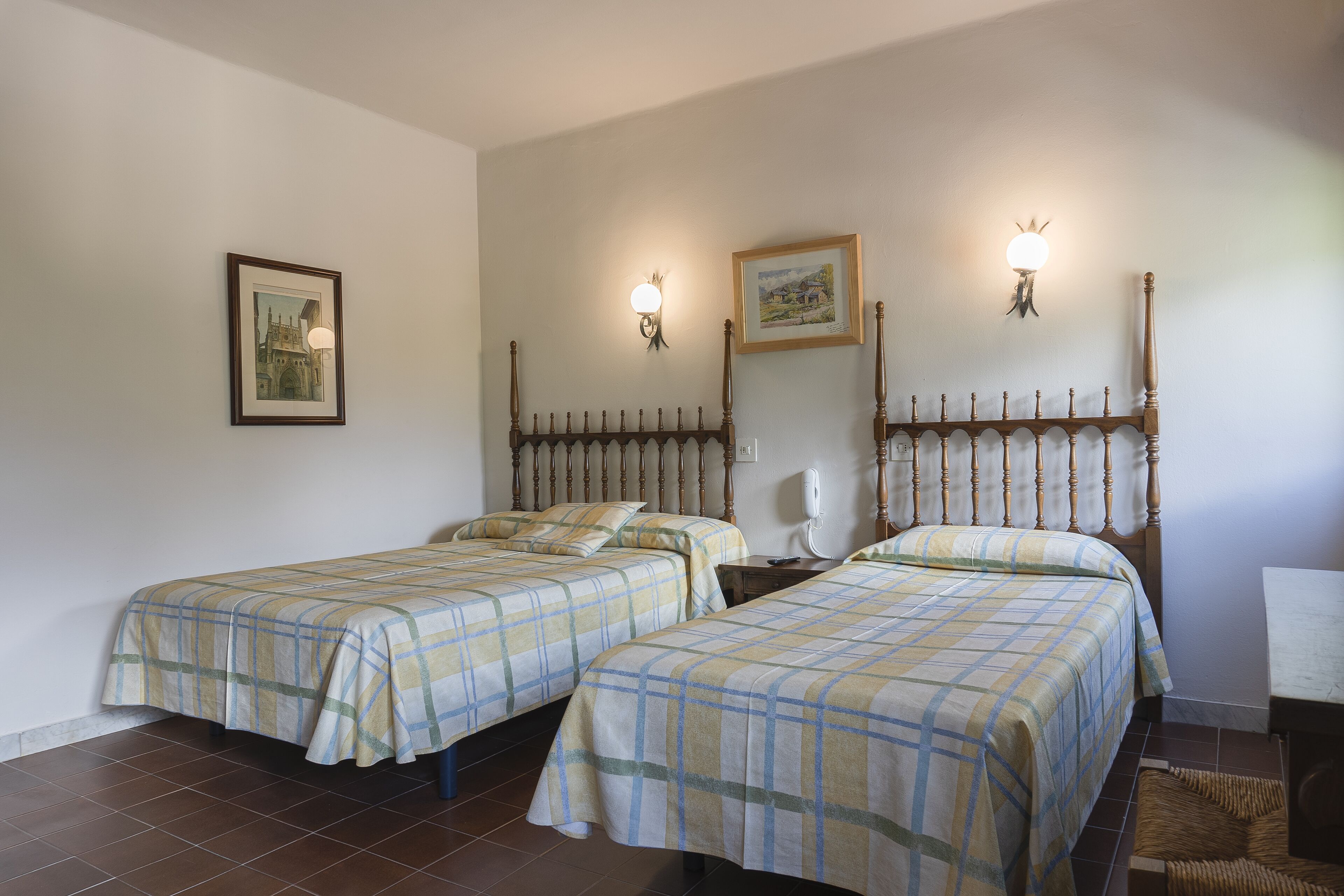 A room with two beds, a wooden headboard, a wall-mounted phone, and a framed picture.
