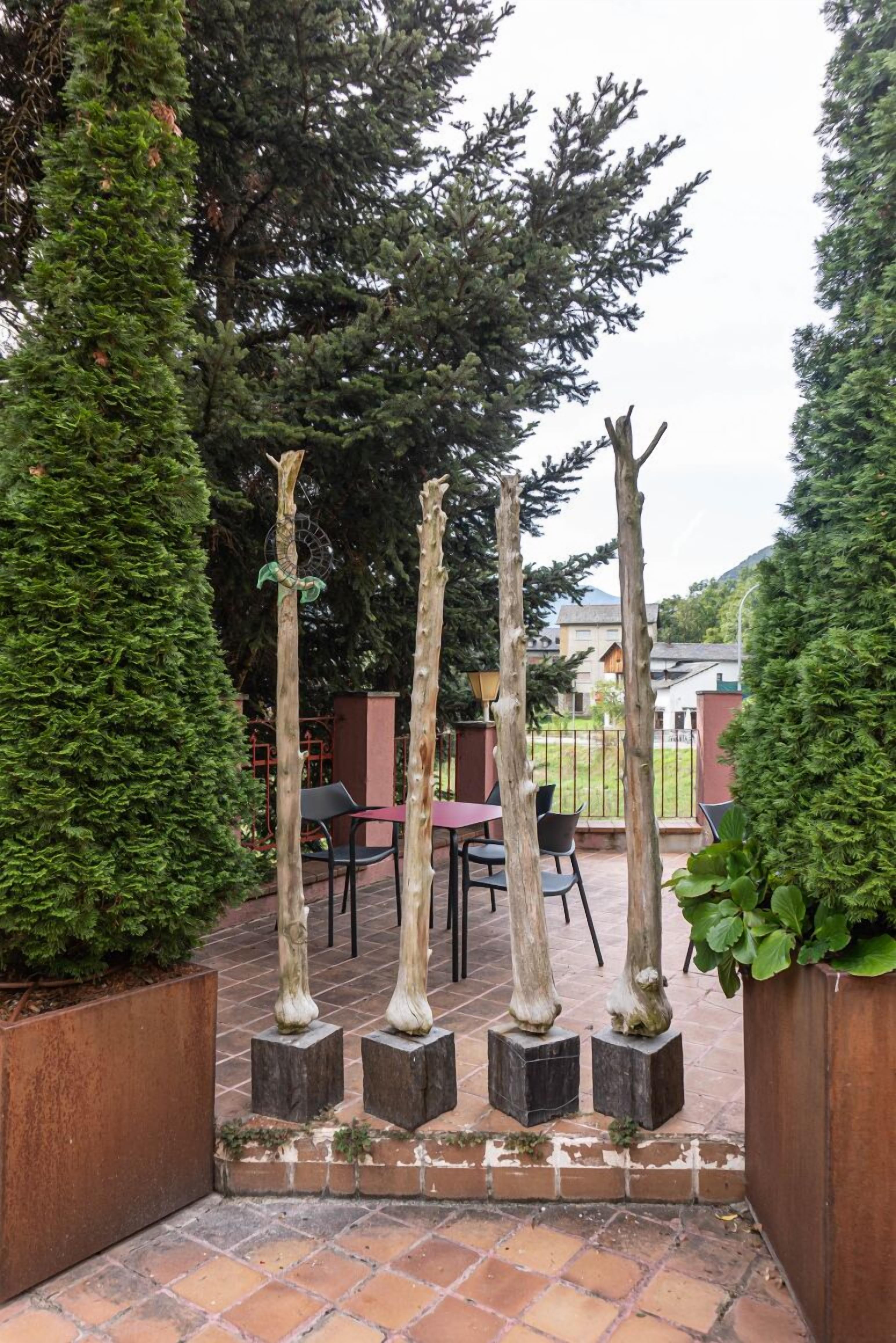 Un patio con suelo de ladrillo, rodeado de árboles altos y delgados y algunas sillas.