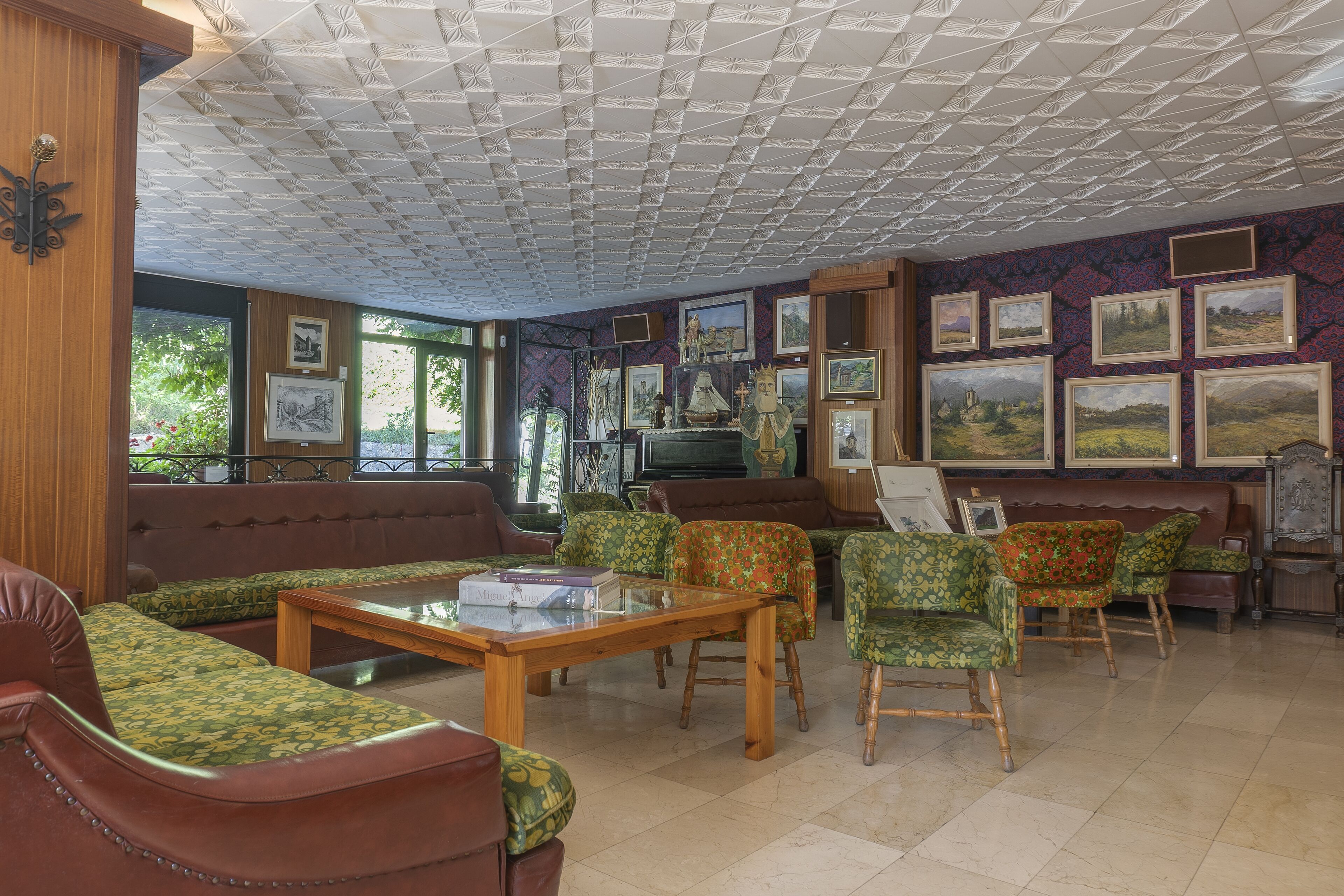 Una habitación con techo de madera, muebles con estampado verde y cuadros en las paredes.