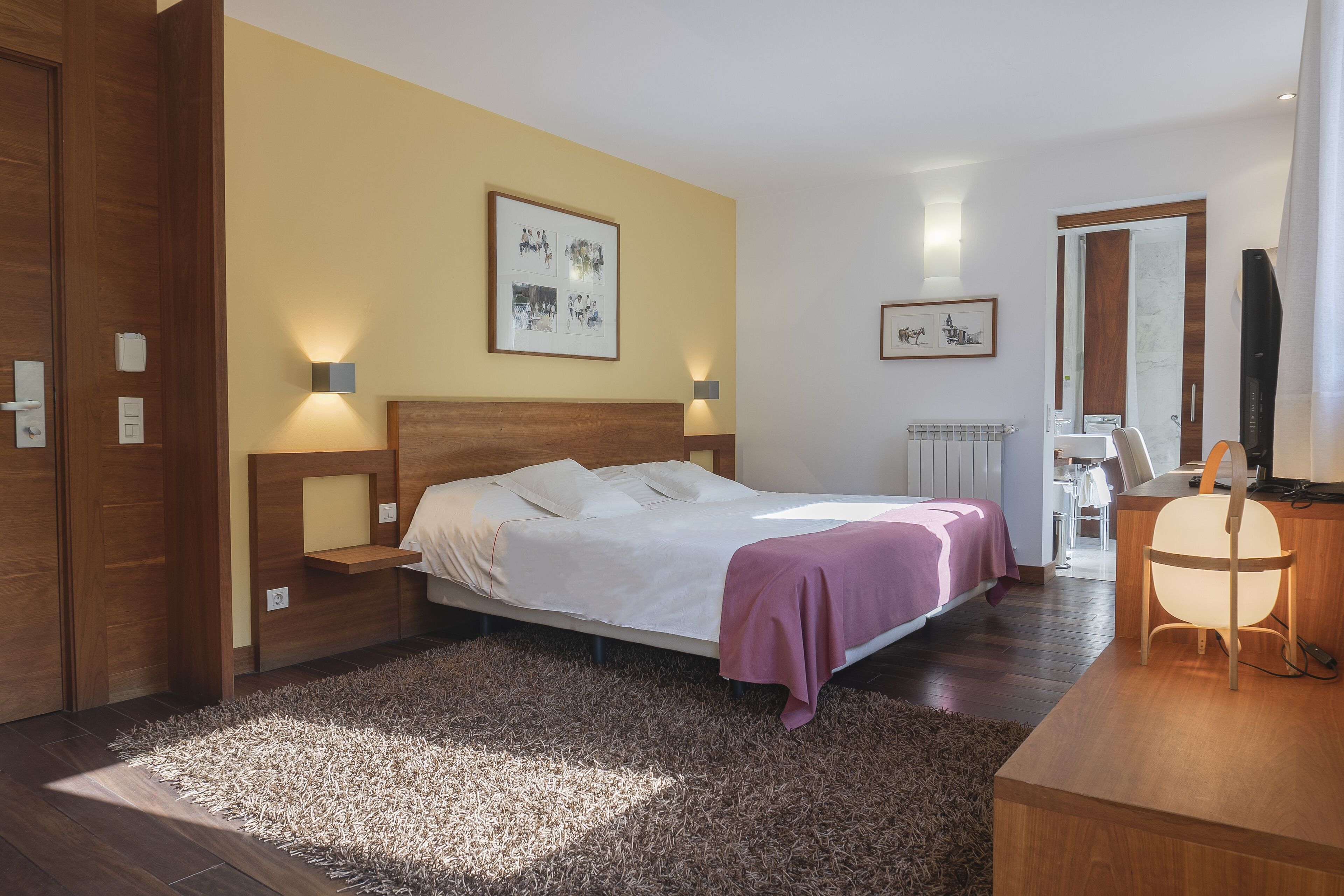 Una habitación de hotel moderna con una cama grande, cabecera de madera, mesitas de noche, un escritorio con una silla y un espejo amplio.
