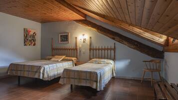 A bedroom with two beds, wooden beams, a wall-mounted light, and a wooden bench.