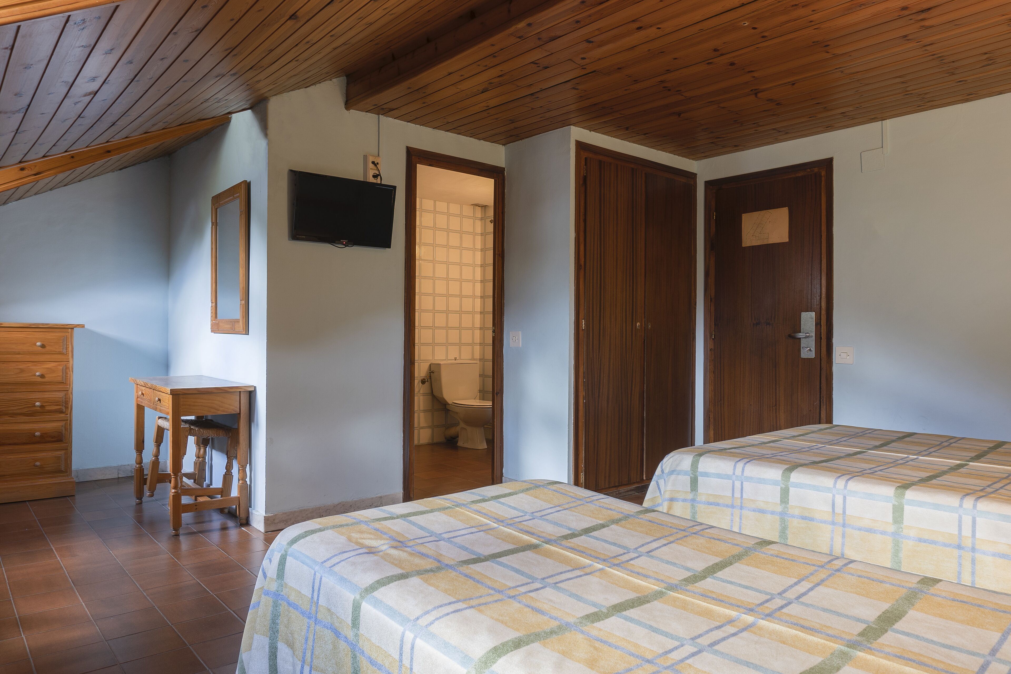 Een slaapkamer met twee bedden, houten meubels, een televisie en een houten plafond.