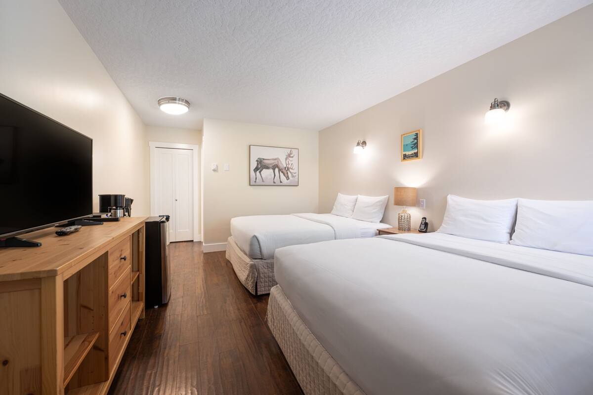 A hotel room with two beds, a wooden desk, a flat-screen TV, and a painting on the wall.