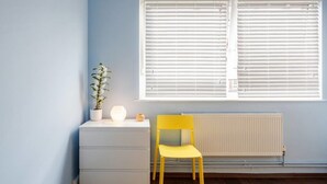 A room with a window, a radiator, a white dresser, a yellow chair, and a potted plant. - Tower Bridge Apartment (London)