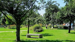 A park with a central concrete bench, surrounded by lush green grass and trees. - Tower Bridge Apartment (London)