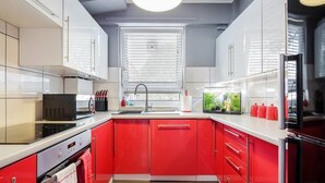 A modern kitchen with red cabinets, a black microwave, and a sink with a window above. - Tower Bridge Apartment (London)
