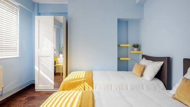 A bedroom with a bed, a bedside table, a nightstand, a window, and a door leading to another room. - Tower Bridge Apartment (London)