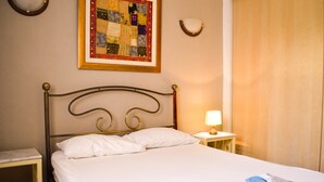 A neatly made bed with white linens, a small bedside table with a lamp, and a framed quilt on the wall. - Cosy Apartment in Sidi Bou Said- Amilcar (Sidi Bou Said)