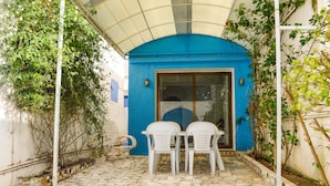 A covered patio with a tiled floor, two white plastic chairs, and a blue wall with a glass door. - Cosy Apartment in Sidi Bou Said- Amilcar (Sidi Bou Said)