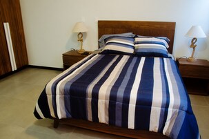 Una cama con colcha a rayas, cabecera de madera, dos mesitas de noche con lámparas y un armario de madera.