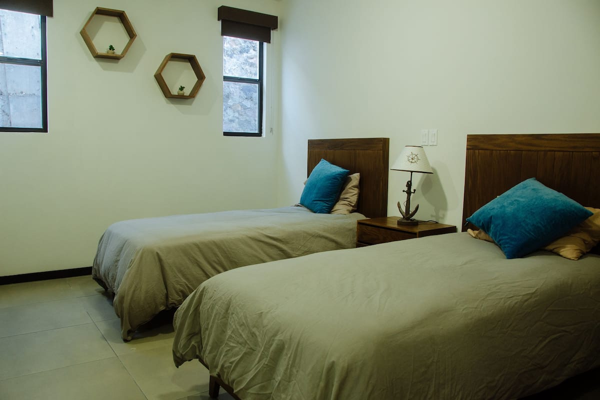 A bedroom with two single beds, a nightstand with a lamp, and two hexagonal mirrors on the wall.