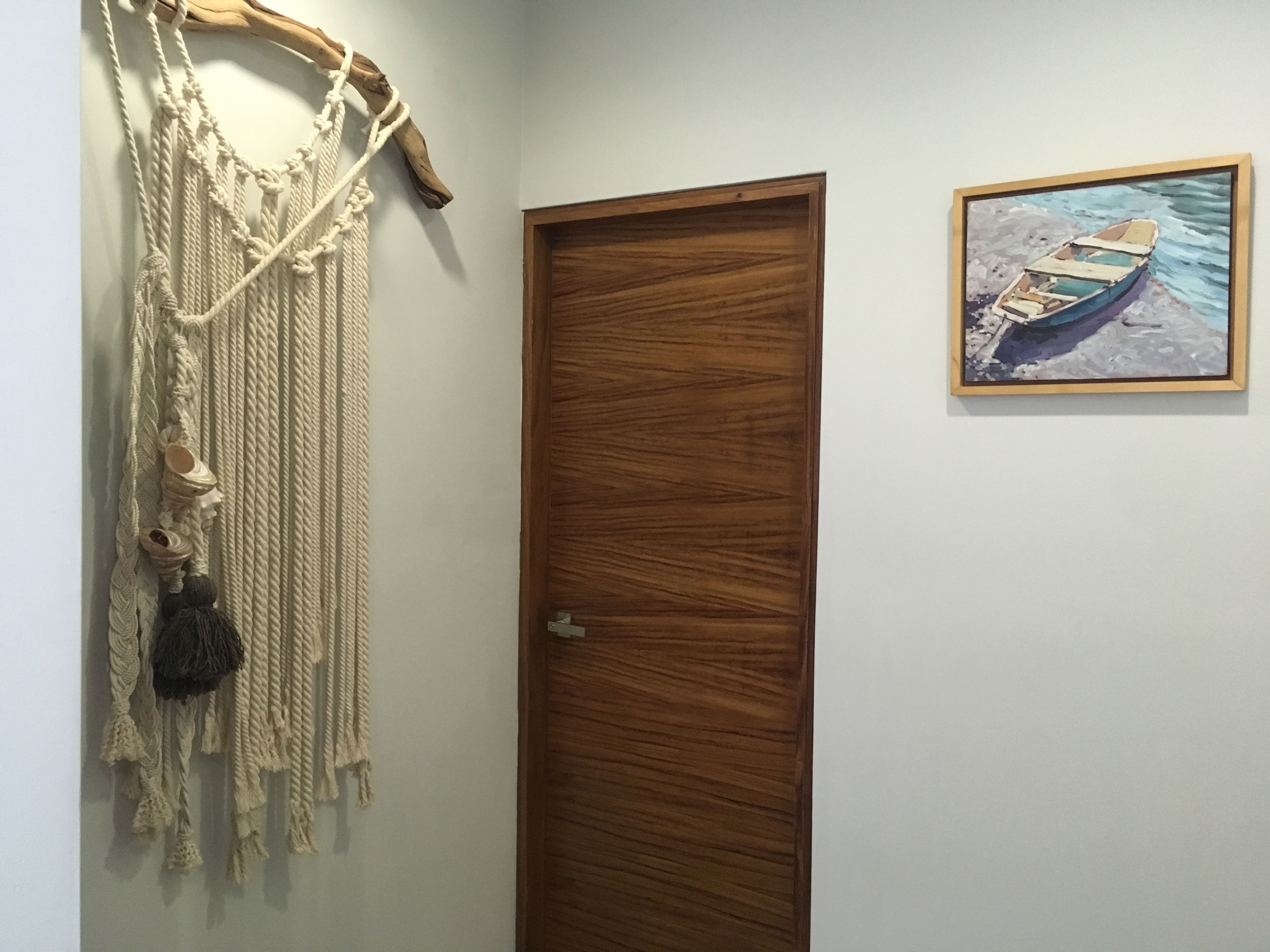 Una puerta de madera con un tapiz de macramé y un cuadro enmarcado de un barco en la pared.