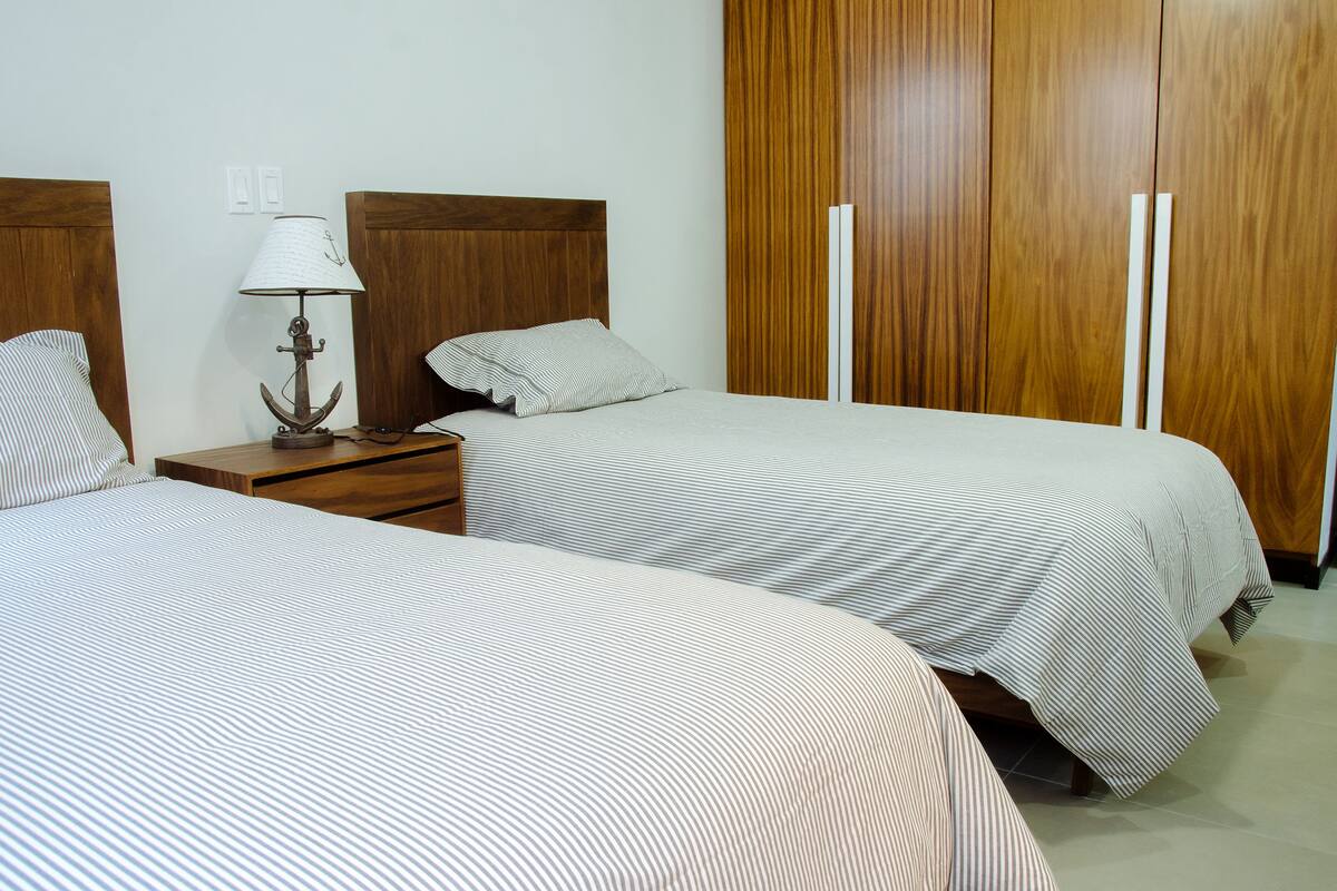 A hotel room with two single beds, a nightstand with a lamp, and a wooden wardrobe.