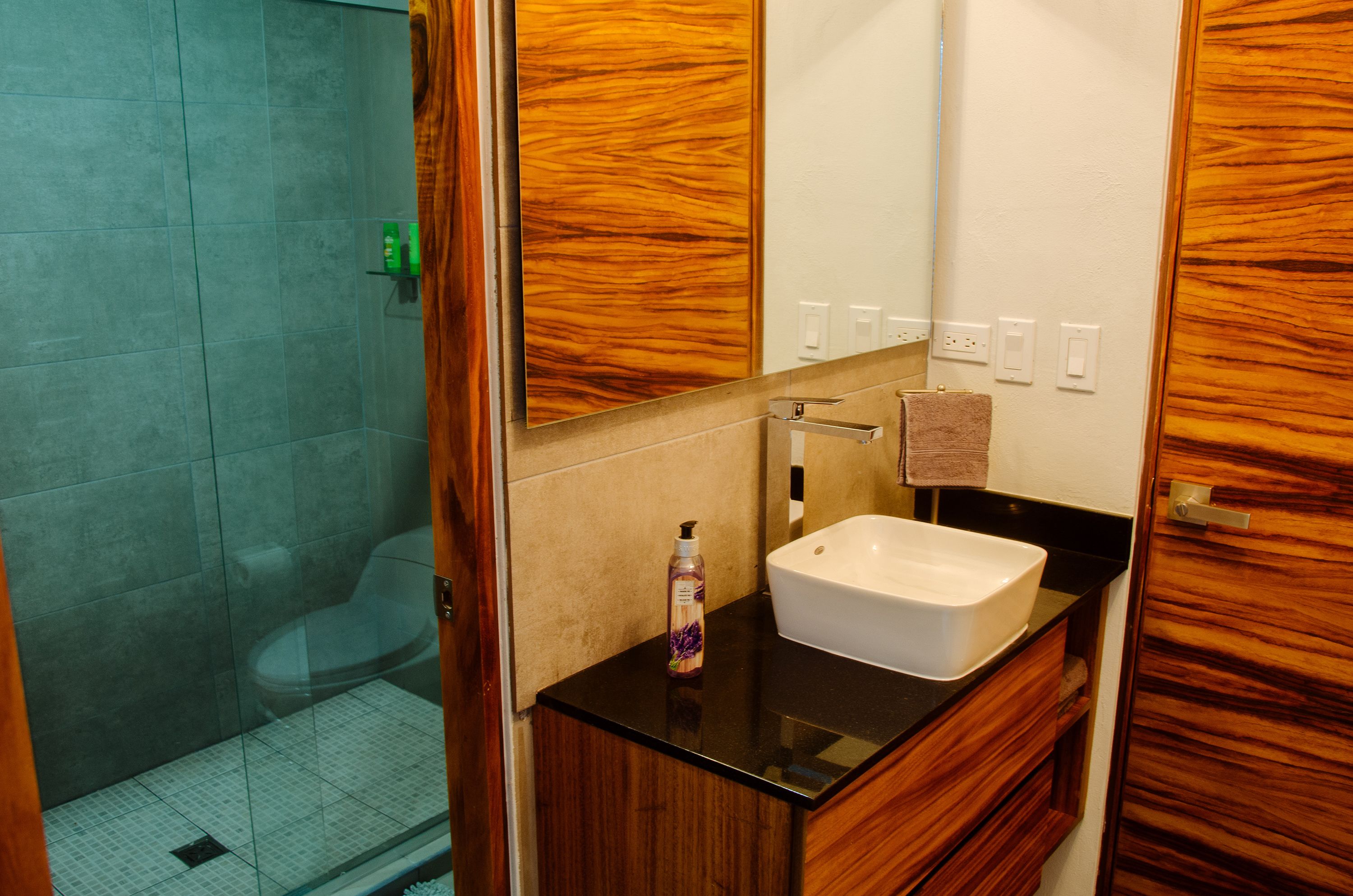 Un baño con tocador de madera, lavamanos blanco y cabina de ducha de vidrio.