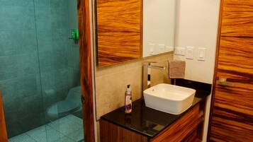 Un baño con tocador de madera, lavamanos blanco y cabina de ducha de vidrio.