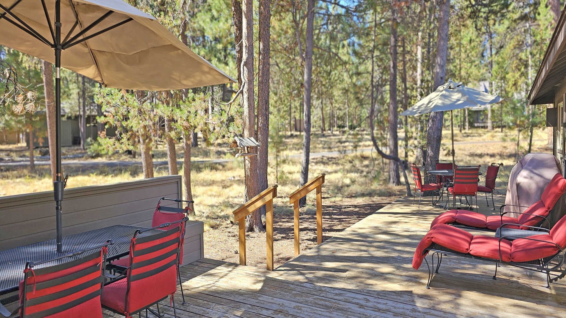 An outdoor deck with wooden flooring, red and black striped chairs, a table, and a covered grill area.