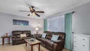 A living room with two brown leather sofas, a wooden coffee table, a white dresser, a ceiling fan, and a cityscape painting on the wall. - Villa Florida Flair - a Quiet Family Paradise in the Heart of Cape Coral (Cape Coral)