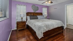 A bedroom with a wooden bed, a ceiling fan, and a heart-shaped wall decoration. - Villa Florida Flair - a Quiet Family Paradise in the Heart of Cape Coral (Cape Coral)