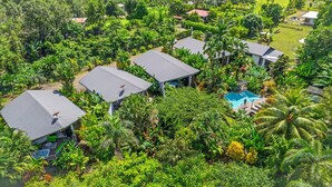 Luchtbeeld van een resort met meerdere gebouwen, een zwembad en weelderige tropische begroeiing.