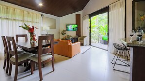 Een moderne woonkamer met een eethoek, een televisie en uitzicht op groen.