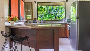 Een moderne keuken met een groot eiland, houten kastjes en uitzicht op weelderige begroeiing.