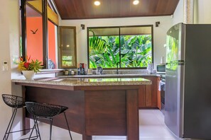 Une cuisine moderne dotée d’un grand îlot central, de meubles en bois et offrant une vue sur une végétation luxuriante.