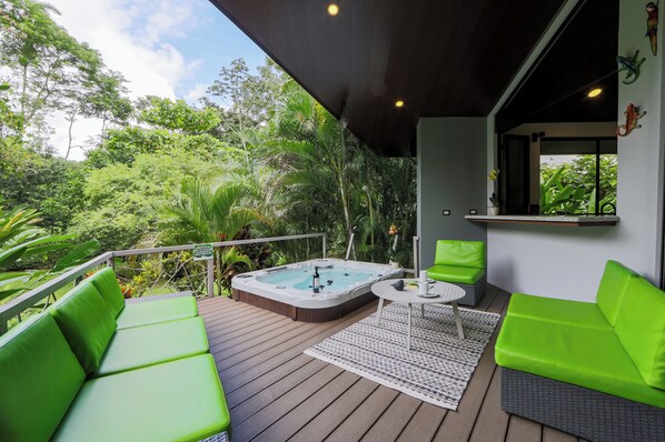 Un bain à remous sur une terrasse en bois, avec des sièges verts et une petite table.