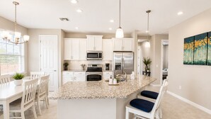 A modern kitchen with white cabinets, a granite island, stainless steel appliances, and pendant lighting.