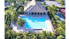 A large house with a swimming pool, surrounded by palm trees and a well-maintained lawn.