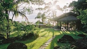 Un jardin tropical avec un sentier en pierre menant à une construction au toit de chaume.