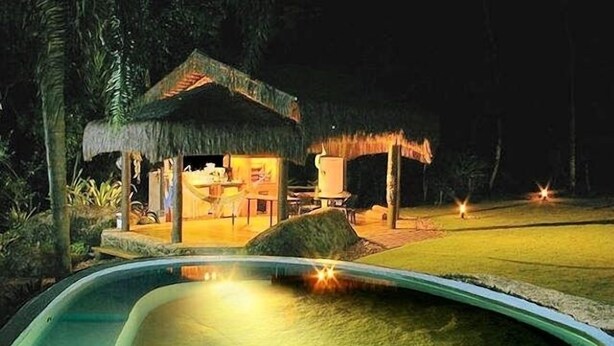 Une piscine avec une structure couverte d’un toit de chaume en arrière-plan.