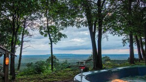 Uma banheira de hidromassagem com uma taça de vinho tinto, cercada por árvores e vista para a paisagem.