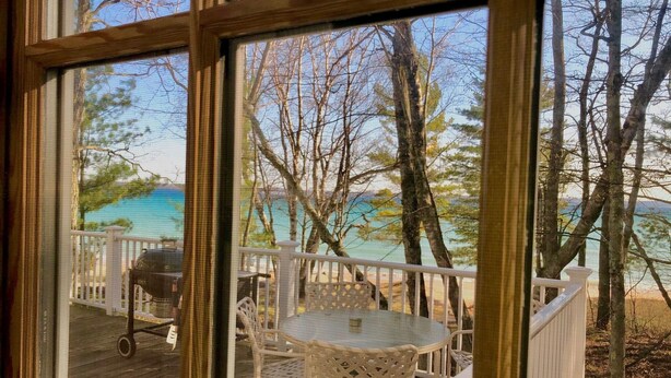 A deck with outdoor furniture, a grill, and a view of the water and trees. - Vacation at "The Boat House", Private Beach, Near Harbor Springs (Harbor Springs)