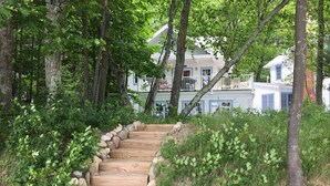 A wooden staircase surrounded by rocks and greenery, leading to a house with blue windows and a white exterior. - Vacation at "The Boat House", Private Beach, Near Harbor Springs (Harbor Springs)