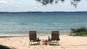 Two beach chairs facing a calm sea with footprints leading to a red bucket and a blue container on the sand. - Vacation at "The Boat House", Private Beach, Near Harbor Springs (Harbor Springs)