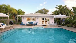 A swimming pool with lounge chairs and umbrellas, surrounded by a house with a patio and tropical plants. - Luxurious Boutique Villa w/ Private Pool, Hot Tub, EV Charger in Heart of Delray (Delray Beach)