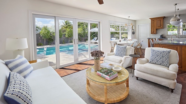 A spacious living room with a large sofa, a round coffee table, and a view of a swimming pool through glass doors. - Luxurious Boutique Villa w/ Private Pool, Hot Tub, EV Charger in Heart of Delray (Delray Beach)