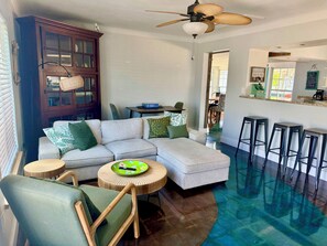 Uma sala de estar com sofá seccional, mesa de jantar, espaço de bar com banquetas e ventilador de teto.