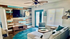 A living room with a sofa, a TV, a ceiling fan, and a wooden wall panel. - BeachHouse Bungalow 🏝Spacious One Level Single Family  Home🏖Walk to the Beach! (Redington Beach)