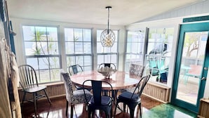 A dining area with a round table, chairs, a hanging light fixture, and large windows. - BeachHouse Bungalow 🏝Spacious One Level Single Family  Home🏖Walk to the Beach! (Redington Beach)